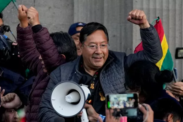 Bolivian President Luis Arce raises a clenched fist surrounded by supporters and media