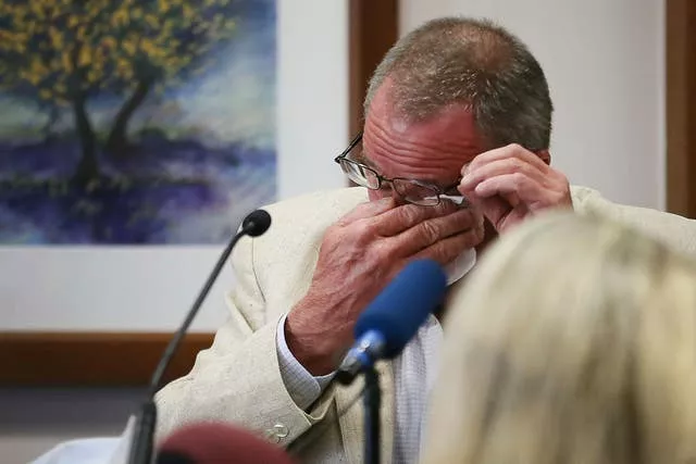 Neil Heslin in cream jacket and glasses in court wiping his eyes